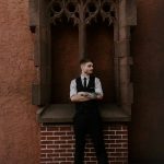 a portrait of a young man against a brick wall with his arms crossed