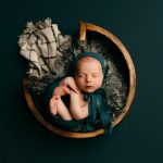 a newborn baby in a wooden bowl swaddled in green fabric