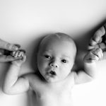 a newborn baby laying on its back holding its parents hands