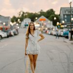 senior portrait photography city lights short white dress walking in street bokeh gilford laconia new hampshire sunset golden hour