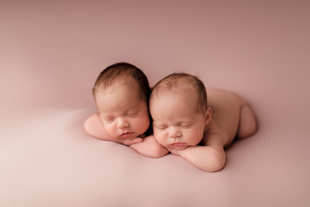 newborn twin girls bum up elbows up dark hair pink backdrop posed concord new hampshire studio