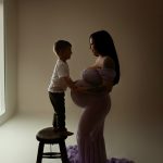 maternity photo of pregnant woman with a child standing on a stool touching her stomach
