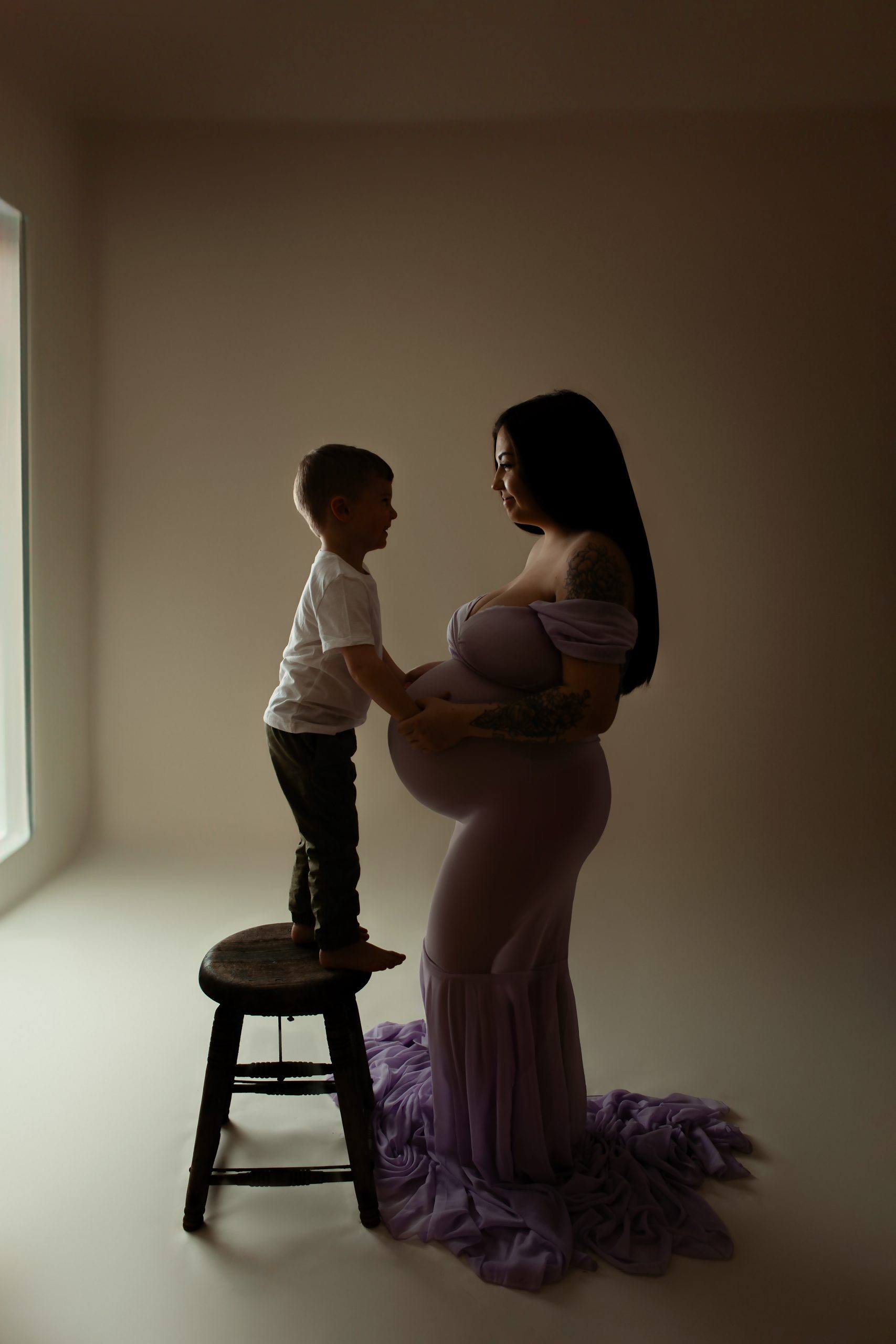 maternity photo of pregnant woman with a child standing on a stool touching her stomach
