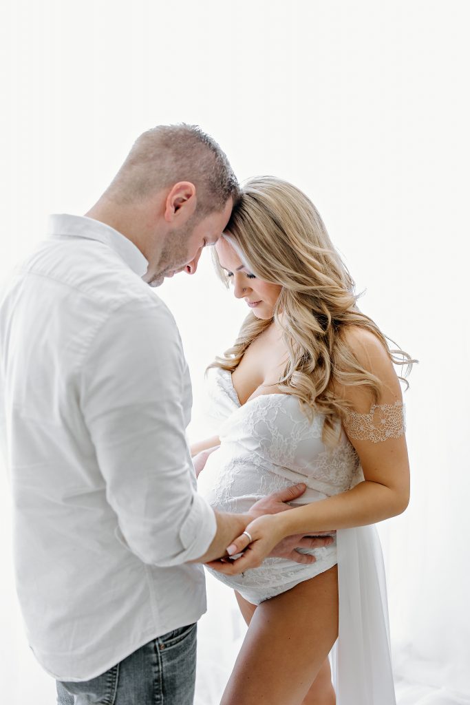 maternity photography husband and wife hands on belly white backlit backdrop blonde hair white dress suit concord new hampshire studio