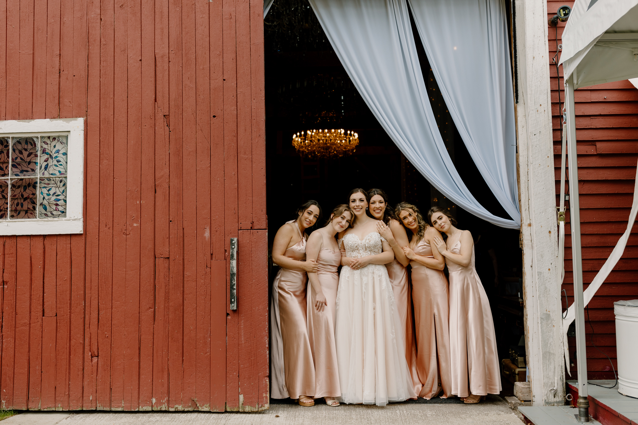 wedding photography bishop farm weddings and events new hampshire wedding venue red barn bridesmaids and bride standing in doorway white curtain chandelier