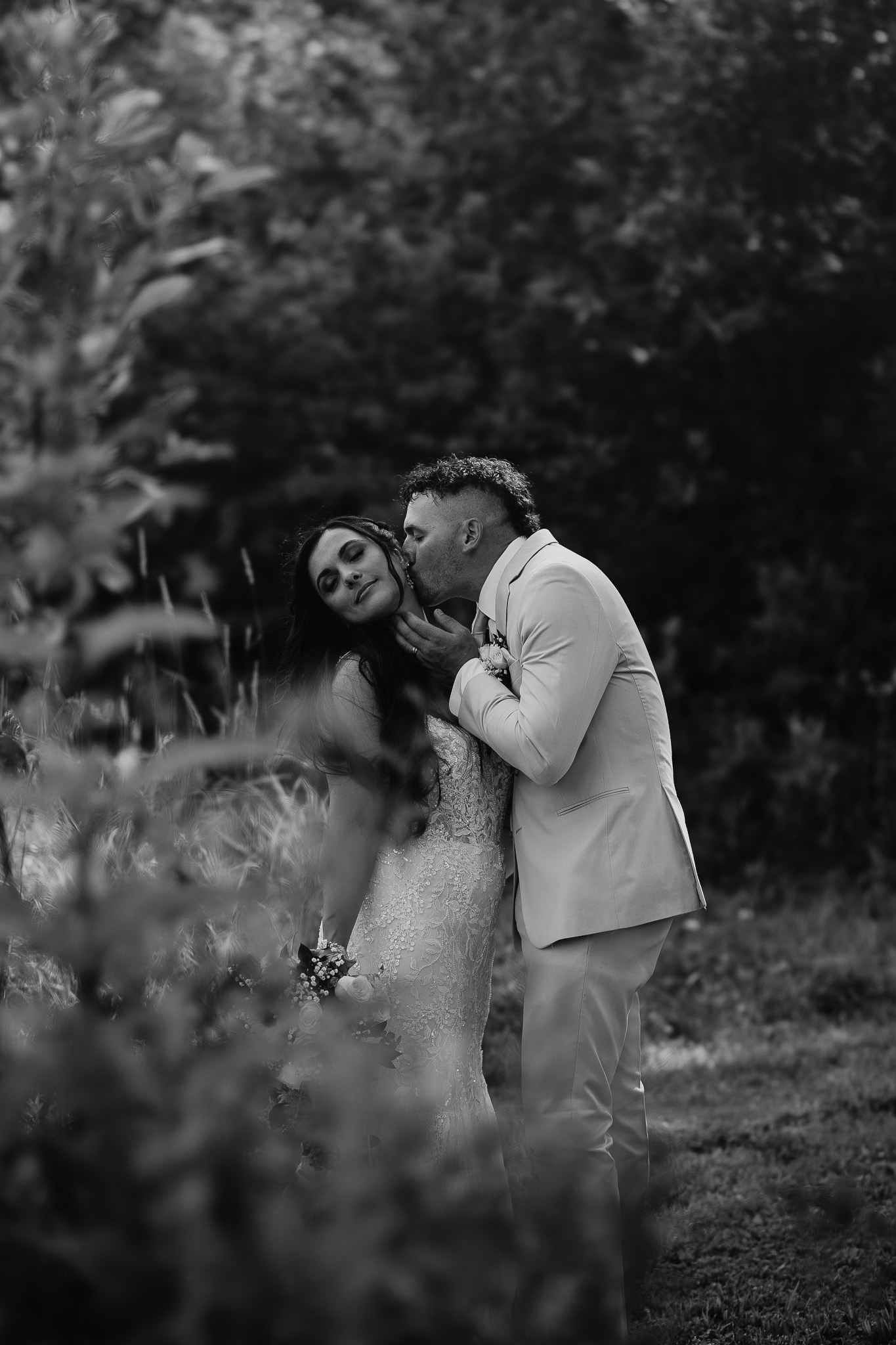 black and white wedding portrait where groom is kissing bride, woods, trees, nh