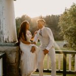 wedding portrait where husband and wife bride and groom are sitting on railing of porch, sunset, golden hour, nh
