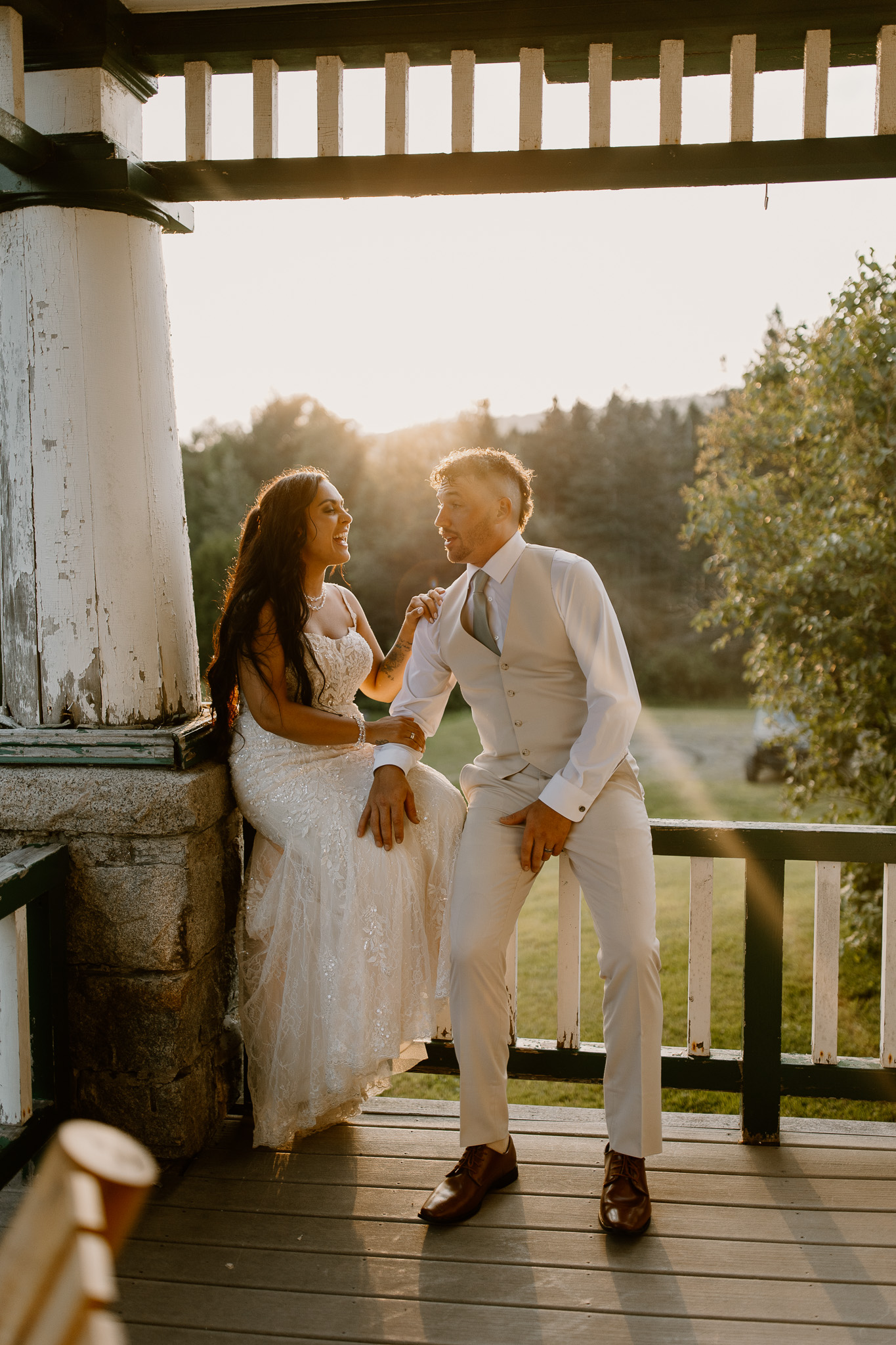 wedding portrait where husband and wife bride and groom are sitting on railing of porch, sunset, golden hour, nh