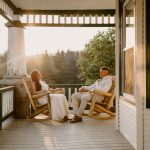 wedding portrait where husband and wife bride and groom are sitting on railing of porch, sunset, golden hour, nh sitting in chairs