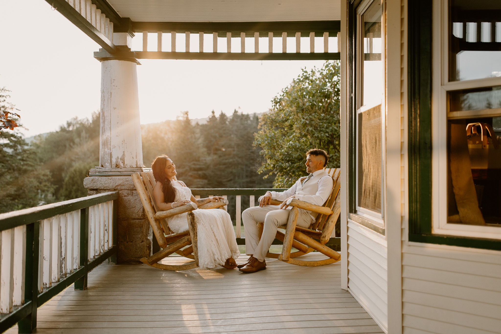 wedding portrait where husband and wife bride and groom are sitting on railing of porch, sunset, golden hour, nh sitting in chairs