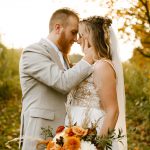 Bride and groom kiss outside a historic white New England home during their fall wedding, surrounded by autumn foliage and fallen leaves.