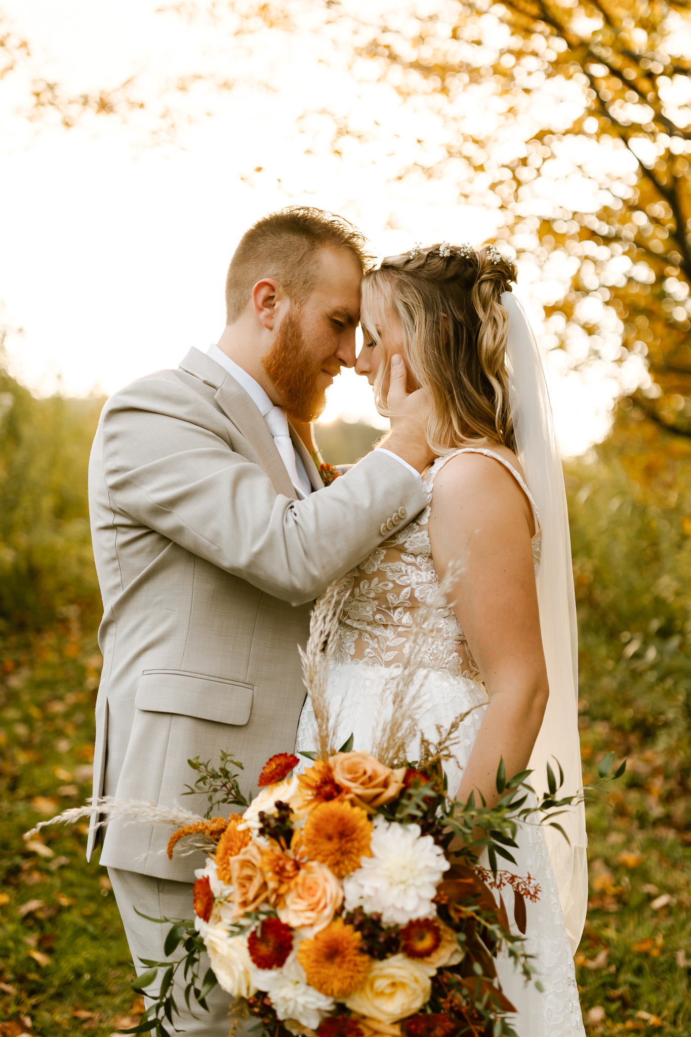 Bride and groom kiss outside a historic white New England home during their fall wedding, surrounded by autumn foliage and fallen leaves.