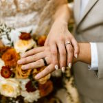 Bride and groom kiss outside a historic white New England home during their fall wedding, surrounded by autumn foliage and fallen leaves.