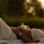 Maternity portrait of a belly where mom is laying down in the grass and holding flowers over her belly, sunset, golden hour, NH