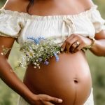 Maternity portrait where focus is on belly, mom's hand on her belly and holding flowers, nh
