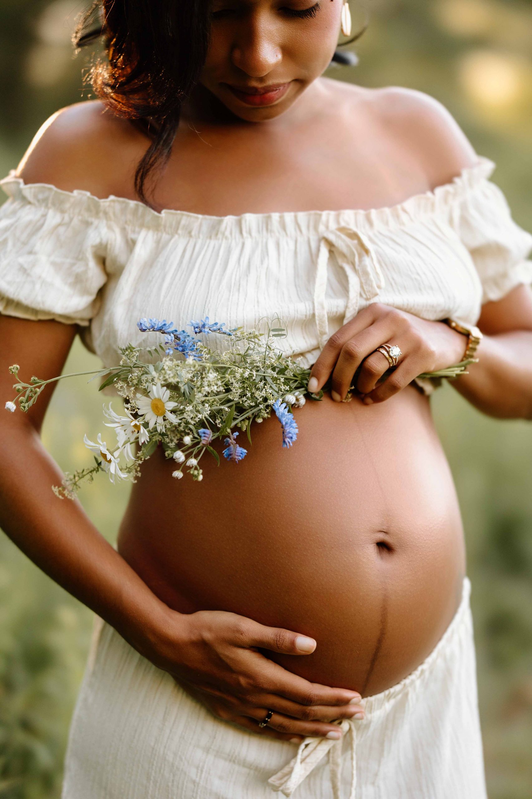 Maternity portrait where focus is on belly, mom's hand on her belly and holding flowers, nh