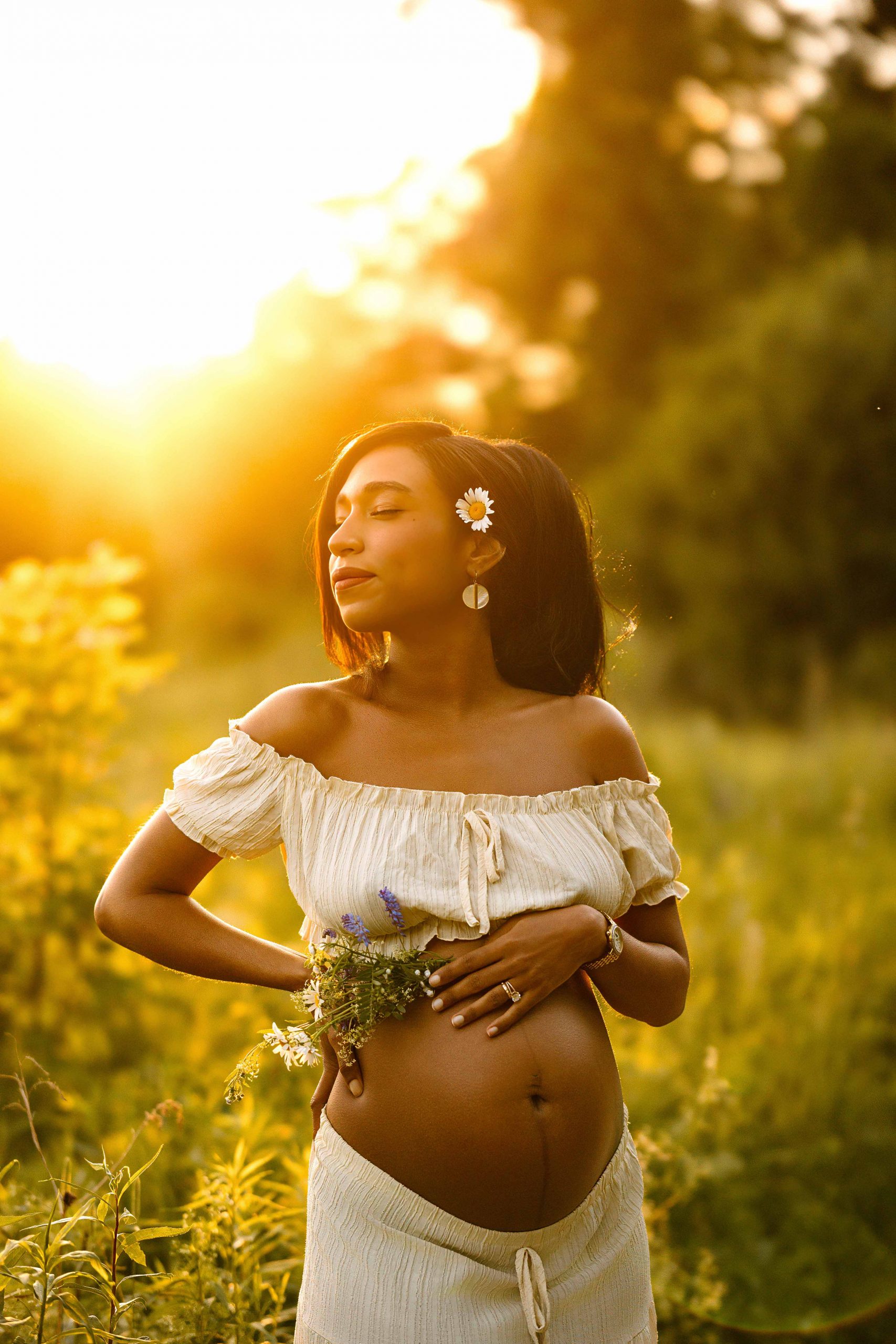 Maternity portrait where focus is on belly, mom's hand on her belly and holding flowers, nh