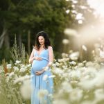 Maternity portrait with mom in blue dress standing with white flowers, golden hour, sunset, NH