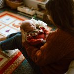 in-home newborn session where baby is sitting on mom's lap in living room