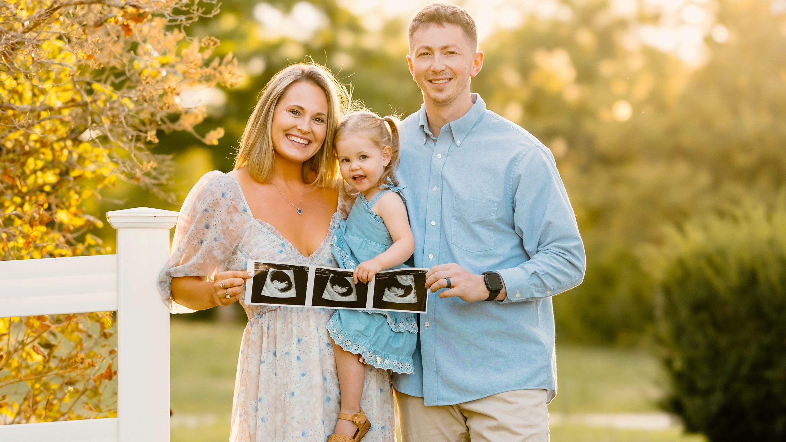 family holding sonogram with toddler at golden hour